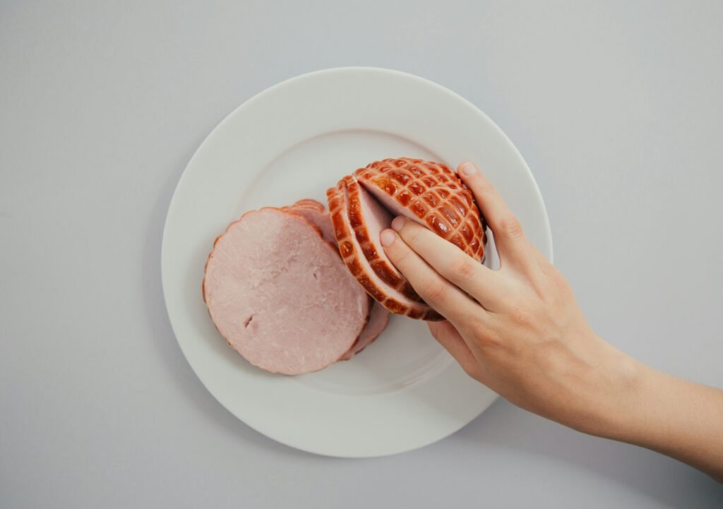 person holding sliced ham in white ceramic plate